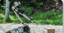 Lance Disrupter mounted on a FLIR PackBot robot on a gravel path, aimed at a package left beside a utility pole