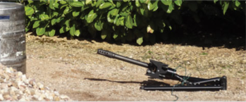 Scabbard Stand deployed low on gravel, the disrupter laid out flat and aimed at a target at stand-off distance